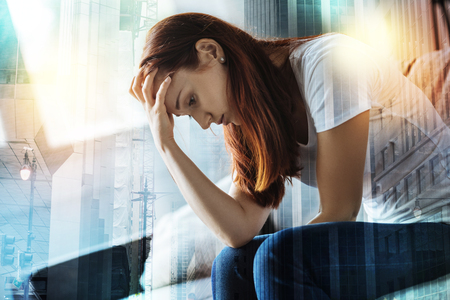 Pretty disappointed redhead woman sitting in the room on the sofa bowing and holding hand near head.の写真素材