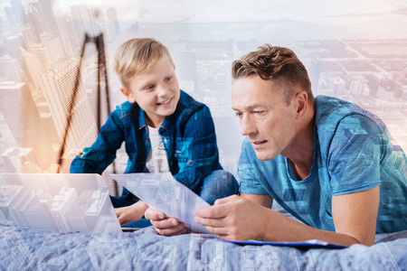 Cheerful man leaning on elbows and looking on paper in both hands while reading exerciseの写真素材