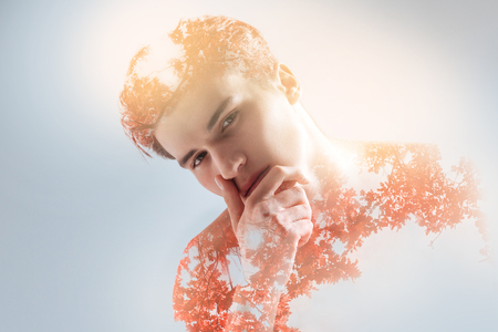 Handsome nice guy touching his face while gazing at the camera and lowering headの写真素材