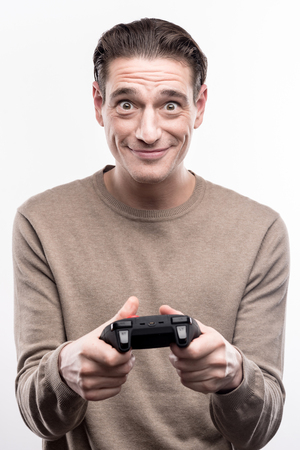 Diligent player. Cheerful handsome man holding a video game controller and widening his eyes, playing enthusiasticallyの写真素材