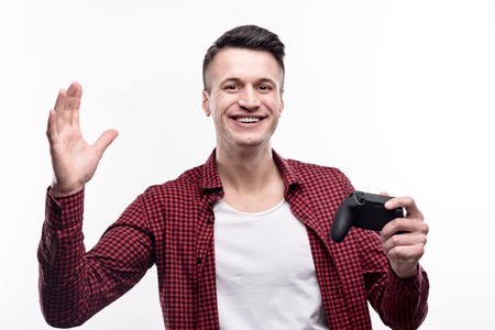 Perfect game. Upbeat handsome young man posing for the camera with a game controller in one hand and waving with the other handの写真素材