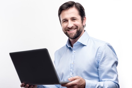 Love my occupation. Charming cheerful middle-aged businessman in a baby blue shirt posing with a laptop while smiling at the camera brightlyの写真素材