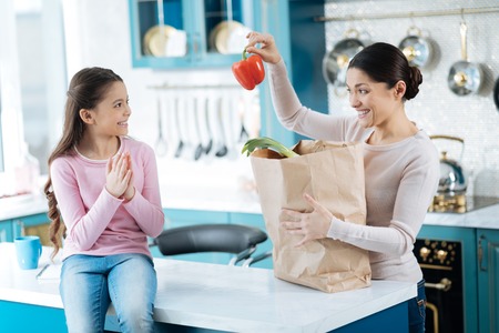 Favourite vegetable. Pretty content dark-haired woman holding a packet and smiling and showing pepper to her happy daughterの写真素材