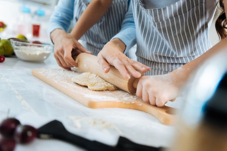 Making cookies. Loving cute little daughter making some dough and her mom helping her and they wearing apronsの写真素材