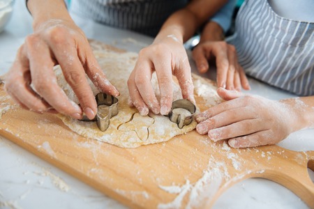 Cute molds. Loving good little daughter making some cookies and using molds while her mom helping her and they wearing apronsの写真素材