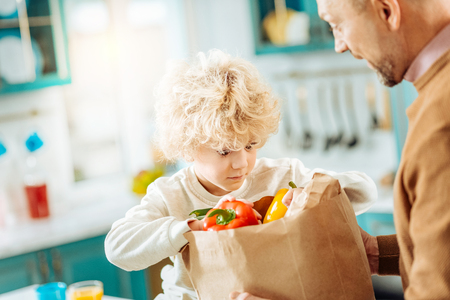 So curious. Cute curly nice boy sitting near his father and looking into the bag while being curious what is in itの写真素材