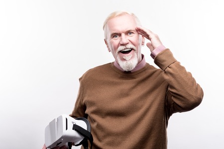Mind-blowing technologies. Upbeat elderly man touching his head, being pleasantly surprised, having used a virtual reality headset for the first timeの写真素材
