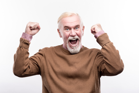 Big success. Pleasant cheerful senior man raising his hands in celebratory gesture and shouting while posing isolated on a white backgroundの写真素材
