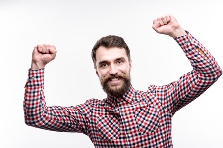 Long-awaited achievement. Charming bearded man raising his hands in triumph, having achieved success, and smiling brightly while posing isolated on a white backgroundの写真素材