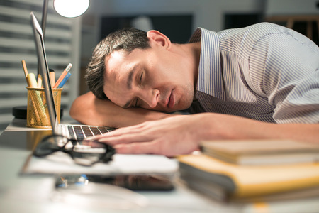 A minute sleep. Appealing cute male employee seeing dreams while resting on the table where laptop...