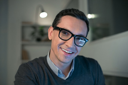 White smile. Cheerful jolly merry man grinning while staring at the camera and putting on glassesの写真素材