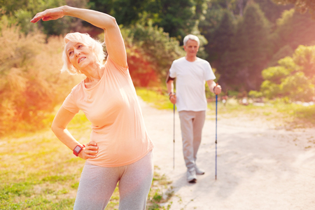 Getting fit. Energetic elderly woman doing exercises in fresh air while standing in front of you and expressing enthusiasmの写真素材