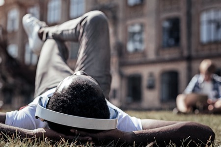 Absolute relaxation. Happy delighted young man lying on the grass and listening to music while wearing headphonesの写真素材