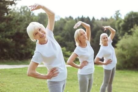 Staying fit. Happy positive aged woman smiling and doing the bending exercise while enjoying it