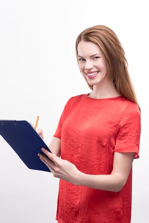 Providing information. Pleasant ginger-haired young woman in a loose red blouse filling in a form on...