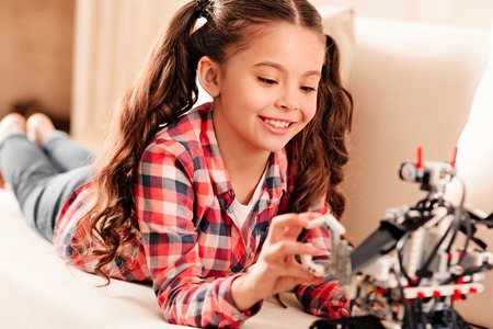Selective focus on a radiant girl with ponytails smiling cheerfully while relaxing on a sofa and...
