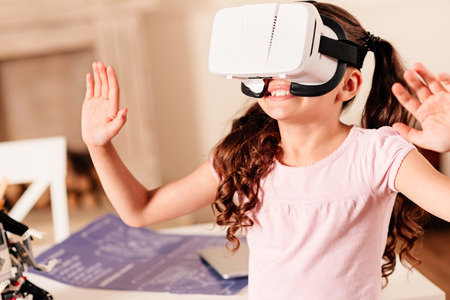 Amazed preteen child gesturing and smiling cheerfully while wearing a VR headset indoors.の写真素材