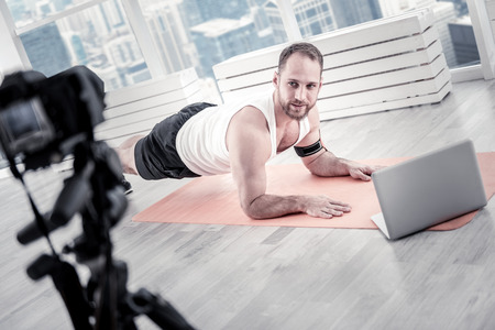 Handsome sportive male blogger performing plank while looking at his camera while recording videoの写真素材