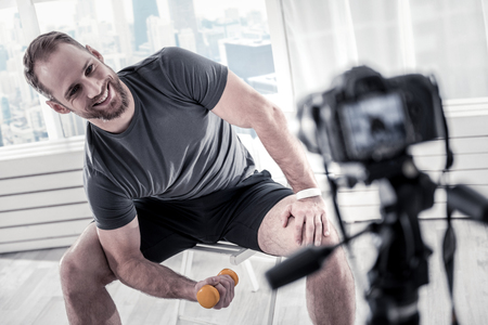 Jolly merry male blogger exercising for perfecting biceps and grinningの写真素材