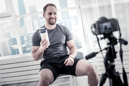 Jolly optimistic male blogger having bottle while smiling and restingの写真素材