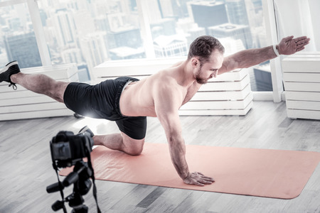Handsome confident male blogger rising hand and leg while training and having blogの写真素材