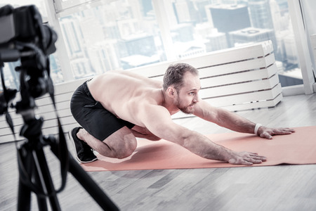 Bearded appealing male blogger training on mat board while filming video for creating blogの写真素材