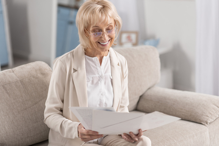 Joyful glad mature businesswoman wearing glasses while examining papers and grinningの写真素材