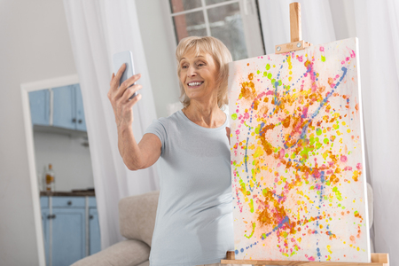 Talented nice mature woman using phone for shooting and easel standingの写真素材