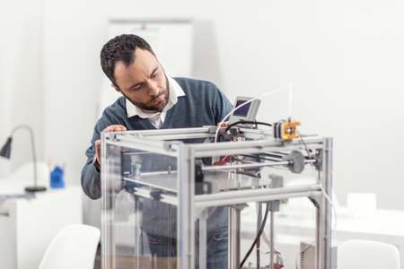 Young professional. Handsome young man checking the work of a 3D printer, looking at the controller...