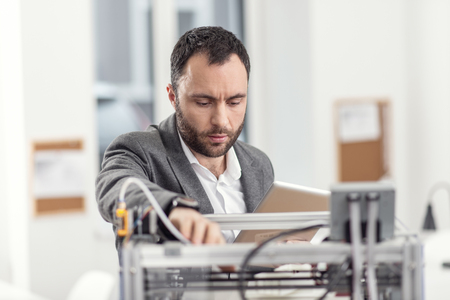 Experienced troubleshooter. Pleasant bristled young engineer using a tablet and trying to fix...