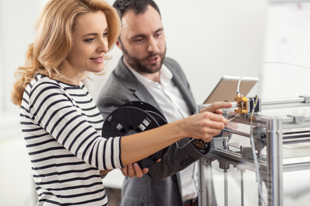 Perfect explanation. Charming senior engineer teaching his female colleague how to insert filament into extruder while the woman holding a spool and following his instructionsの写真素材