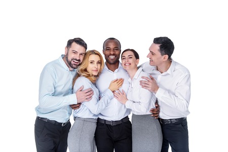 My friends. Good-looking glad stylish young co-workers smiling and hugging and wearing white shirtsの写真素材