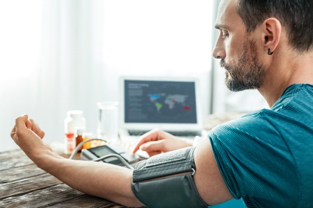 Serious unshaken concentrated man sitting in the bright room by the table measuring pulse looking at hand.の写真素材