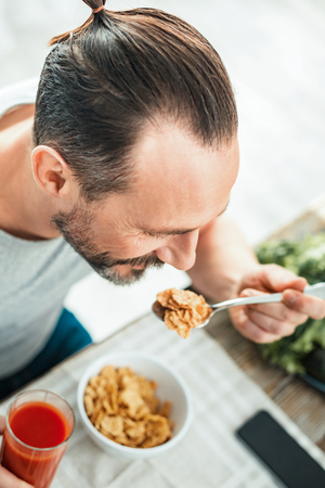 Calm unshaken gay man sitting by the table holding a spoon of flakes and having breakfast.の写真素材