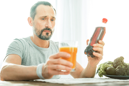 Confused thoughtful man sitting in the bright room holding and overlooking drinks.の写真素材