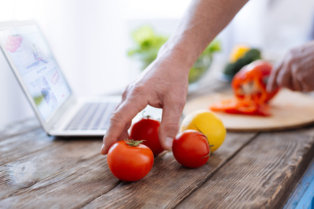Selective focus of charming strong male hands getting tomato for practicing biohacking diet and preparing lunchの写真素材