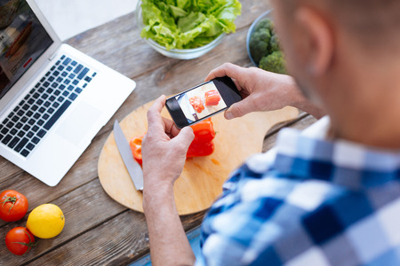 Close up of male hands holding phone while shooting food which lying on wooden surfaceの写真素材