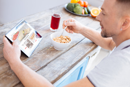 Handsome stylish adorable man examining blog about biohacking while looking at screen and consuming granolaの写真素材