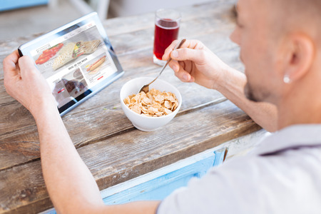 Skillful ambitious man eating healthy granola while taking spoon and studying article about biohackingの写真素材
