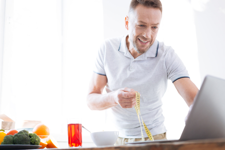 Cheerful attentive man transferring data in program for biohacking while holding metre ruler and smilingの写真素材