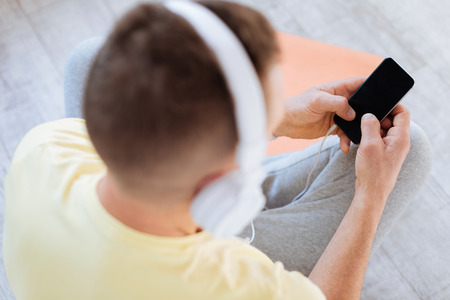 Top view on modern gadget hold by male young hands while man wearing headphonesの写真素材