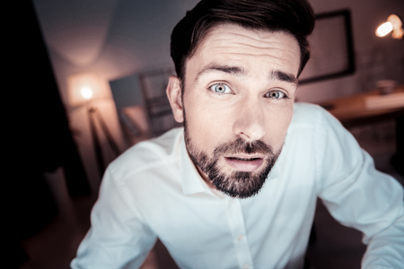 Whats wrong. Interested disappointed unshaken man spending time in the specious room looking straight and having question.の写真素材