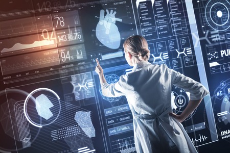 Medical research. Clever enthusiastic progressive doctor carefully touching the transparent screen while using amazing futuristic technologies in her workの写真素材
