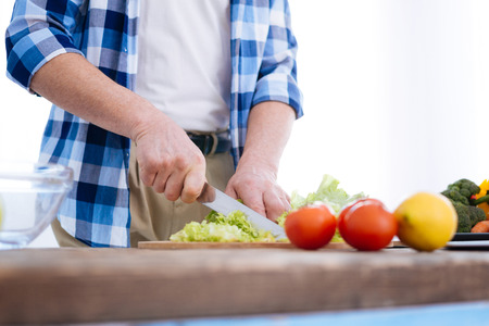 Health benefits. Tender smooth male hands holding knife while chopping salad and cooking dinnerの写真素材