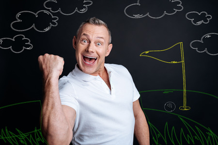 Happy winner. Positive excited young man looking extremely happy and expressing his emotions while winning a very important golf gameの写真素材