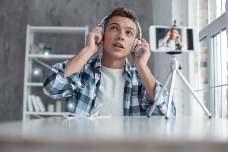 Quality sound. Attractive delighted well-built blogger wearing his headphones and relaxing while making a videoの写真素材