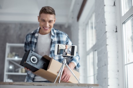 Great sound. Attractive joyful professional well-built blogger holding loudspeakers and smiling while making a videoの写真素材