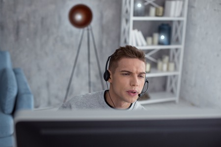 I love games. Handsome concentrated fair-haired teenager looking attentively and wearing headphones while playing computer gamesの写真素材