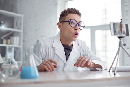 I love chemistry. Nice excited fair-haired teenager wearing a uniform and glasses and smiling while making a videoの写真素材