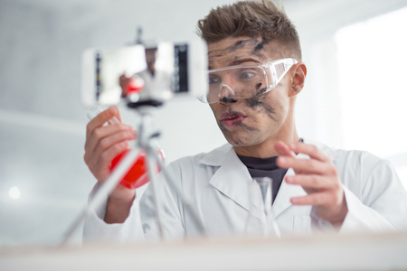 I am angry. Good-looking baffled fair-haired young blogger wearing uniform and holding a test tube while making new videoの写真素材